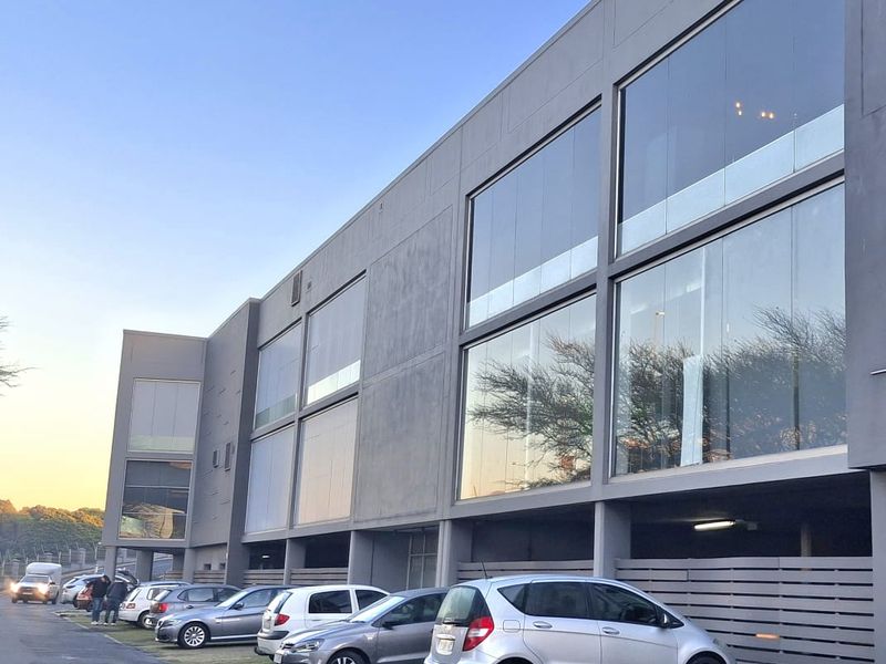 Modern multi-story office building featuring a sleek concrete facade, expansive glass curtain walls, and a convenient ground-level covered parking area.
