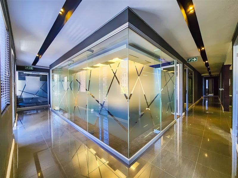 Modern office interior featuring glass-partitioned meeting rooms, polished tile flooring, and recessed ceiling lighting in a professional corporate environment.