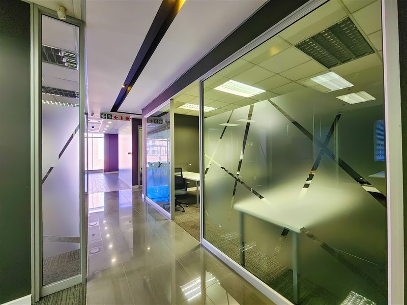 Modern office hallway featuring glass-partitioned meeting rooms with frosted privacy film, recessed ceiling lighting, and polished tile flooring.