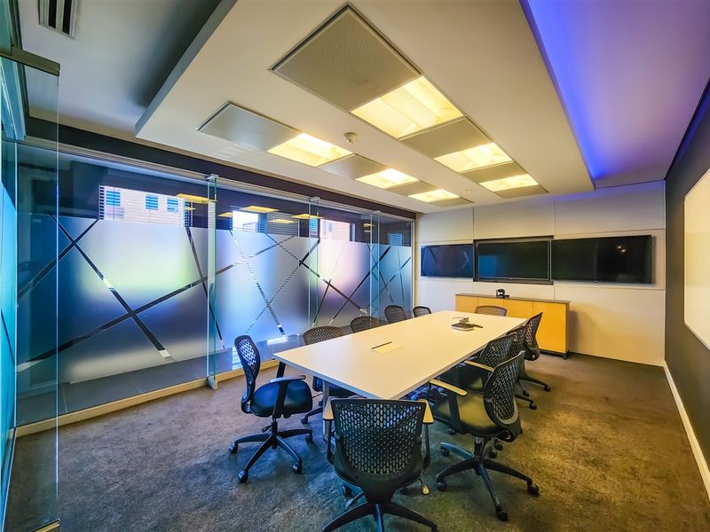 Modern professional boardroom featuring a large conference table, integrated wall-mounted screens, recessed ceiling lighting, and glass partition walls with privacy film.