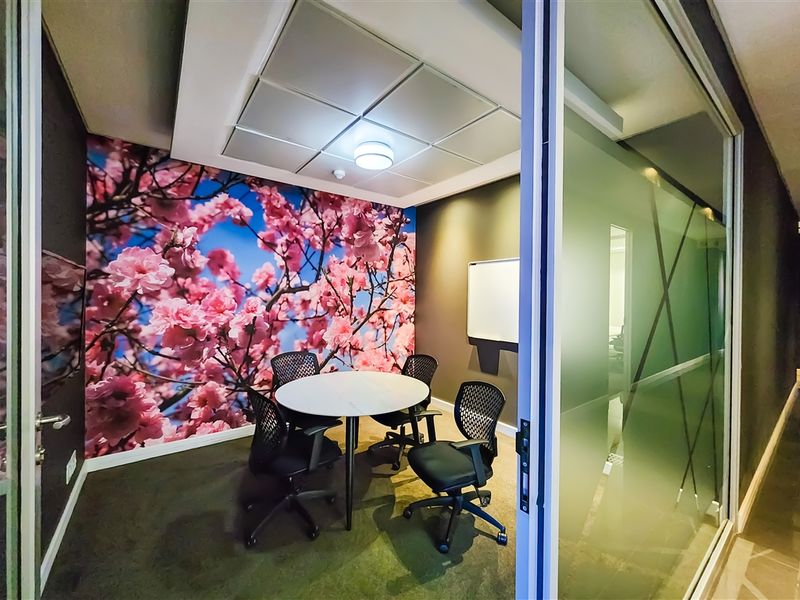 A modern office meeting room featuring a drop ceiling, glass partition wall, and a decorative floral feature wall.