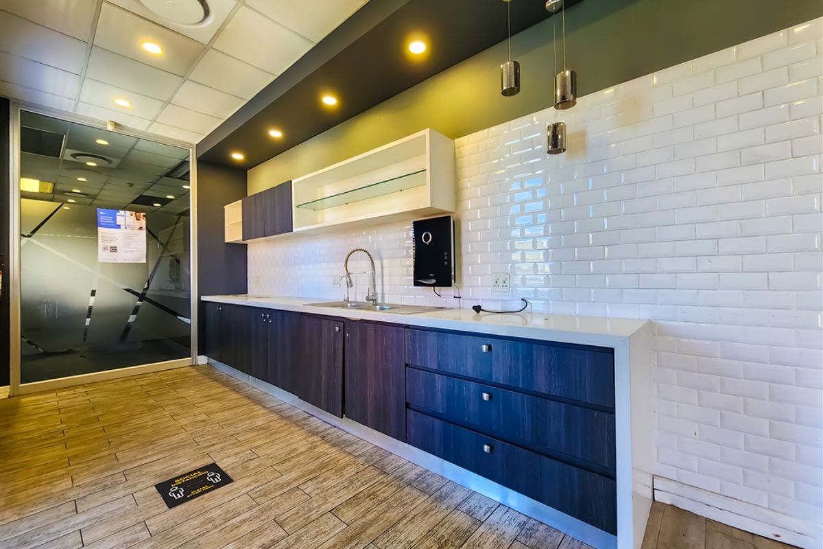 Modern office kitchenette featuring dark wood cabinetry, white subway tile backsplash, stone countertops, stainless steel sink, and recessed ceiling lighting.