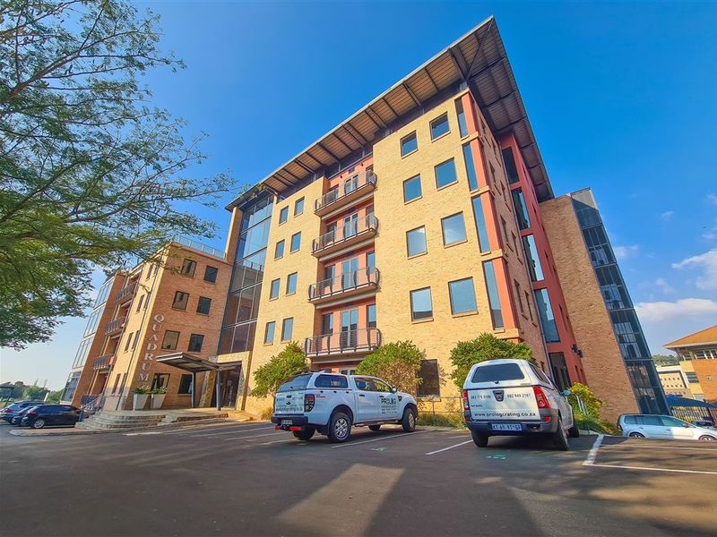 A professional exterior view of the Quadrum office building, showcasing its multi-story brick facade, modern architectural design, and dedicated parking area.