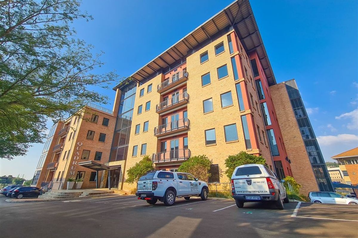 A professional exterior view of the Quadrum office building, showcasing its multi-story brick facade, modern architectural design, and dedicated parking area.