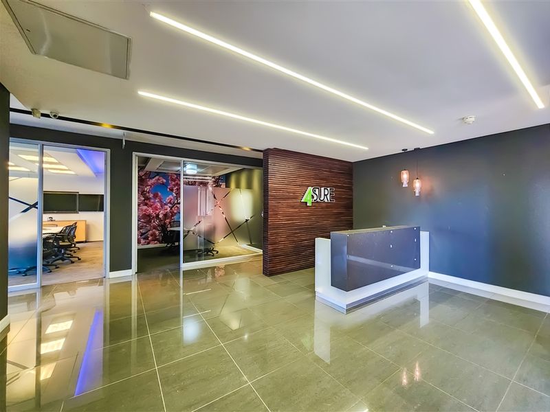 Modern office reception area featuring a sleek built-in reception desk, polished tile flooring, recessed linear lighting, and glass-partitioned office spaces.