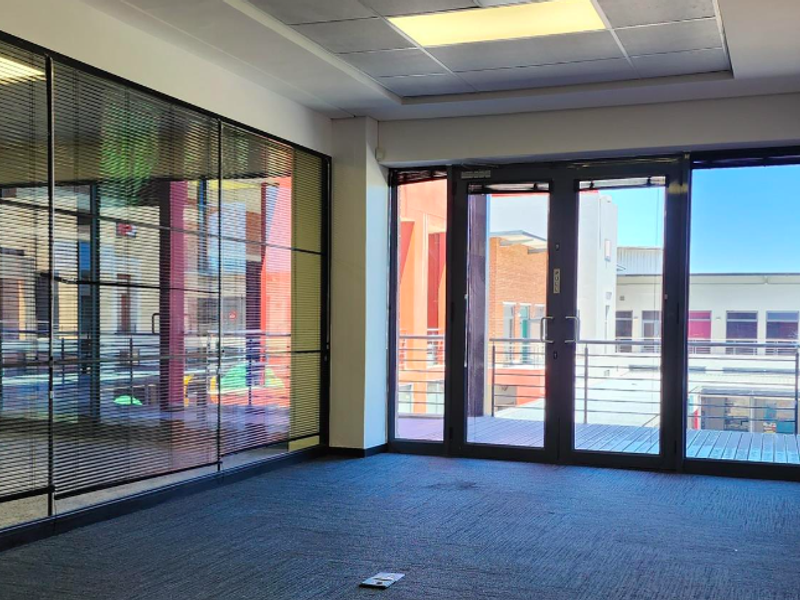 Empty office space featuring a glass partition wall, carpeted flooring, recessed ceiling lighting, and direct access to a private balcony.