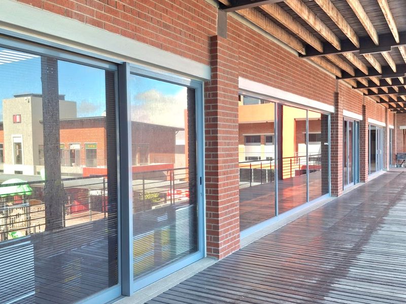 A spacious covered balcony featuring timber decking, exposed ceiling beams, and large sliding glass doors providing access to the office interior.