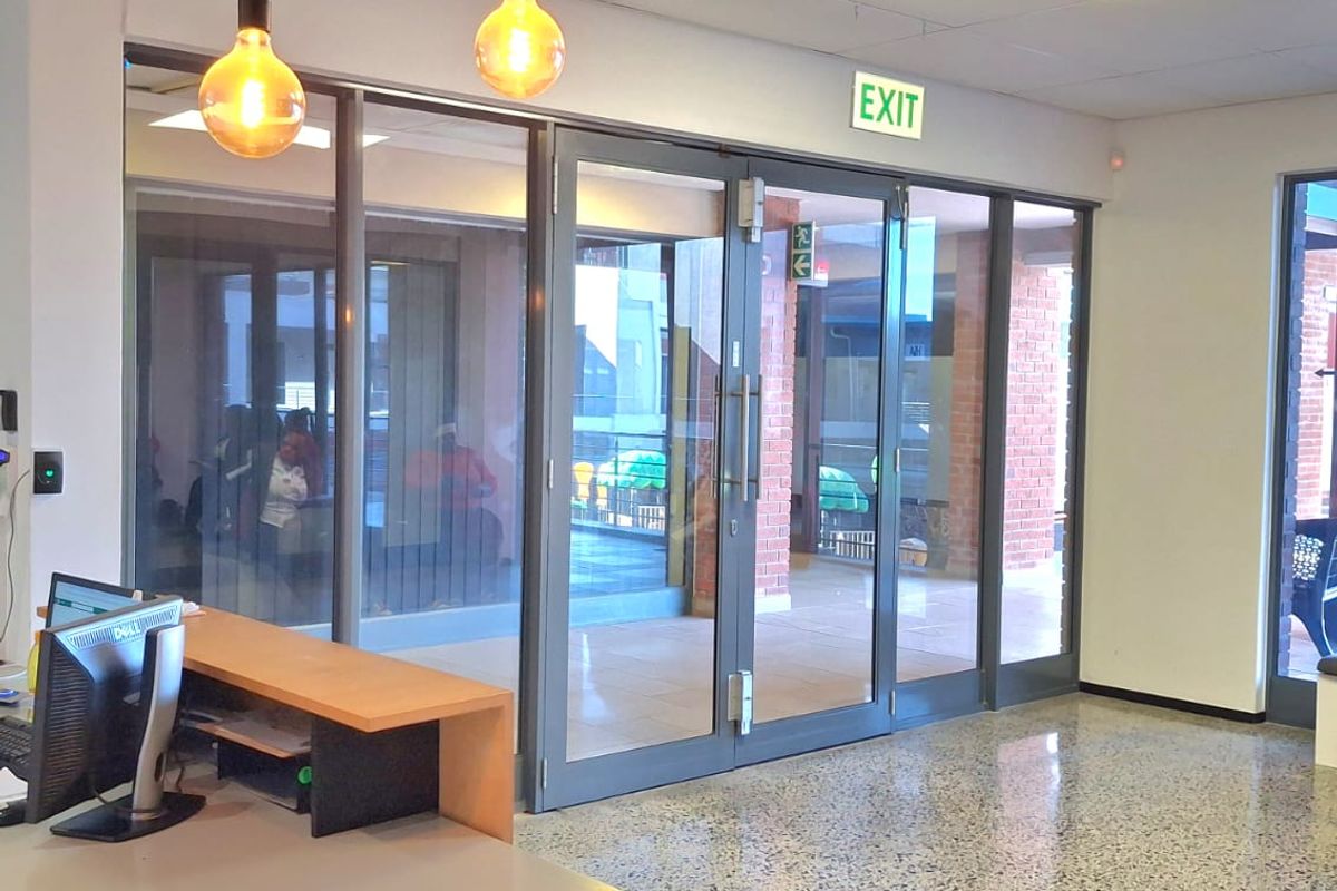 Modern office reception area featuring polished terrazzo flooring, suspended ceiling with recessed lighting, and large aluminium-framed glass doors leading to the exterior.