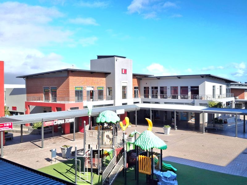 An elevated view of a commercial office complex courtyard featuring paved walkways, covered corridors, and a central playground area.