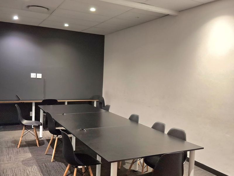 A modern office meeting room featuring recessed ceiling lighting, carpeted flooring, and a neutral color palette with a dark accent wall.