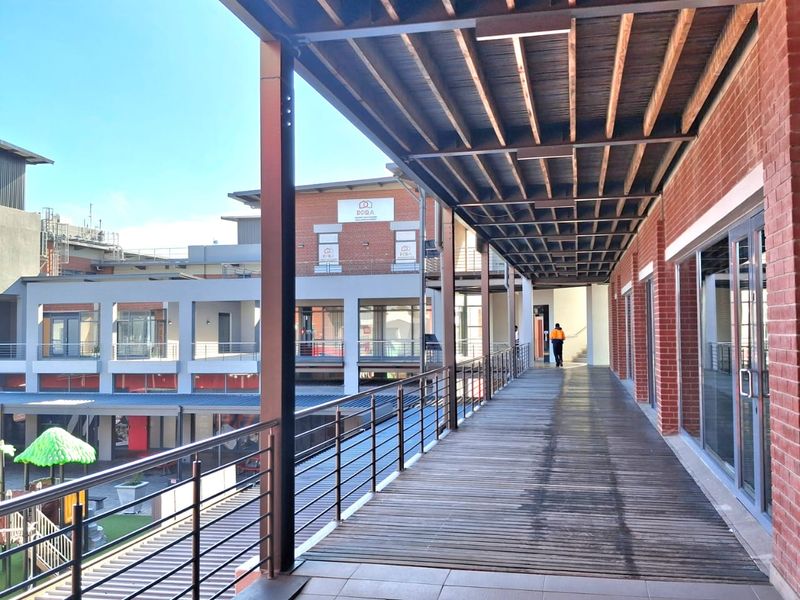 A covered outdoor walkway featuring timber decking, exposed beam ceiling, and metal railings, overlooking an office courtyard area.