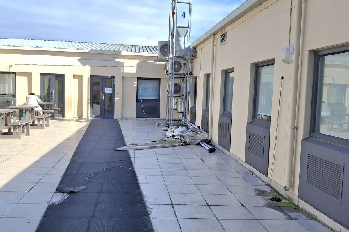 An exterior rear patio area featuring tiled flooring, external HVAC units, and a ventilation stack, with some visible wear to the floor surface.