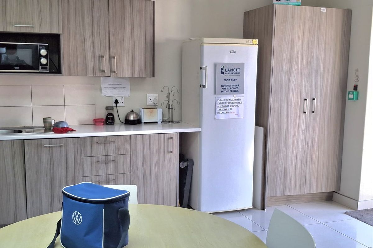 A functional office kitchenette featuring wood-grain cabinetry, laminate countertops, a built-in microwave, and a wall-mounted air conditioning unit.