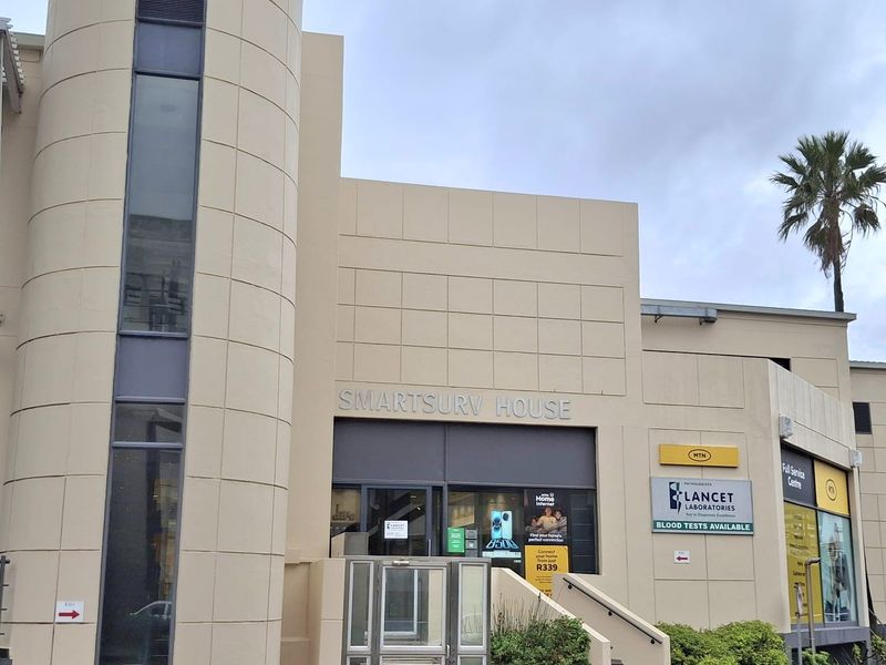 Front facade of Smartsurv House, a commercial office building featuring a prominent cylindrical architectural element, glass entrance, and integrated signage for multiple tenants.