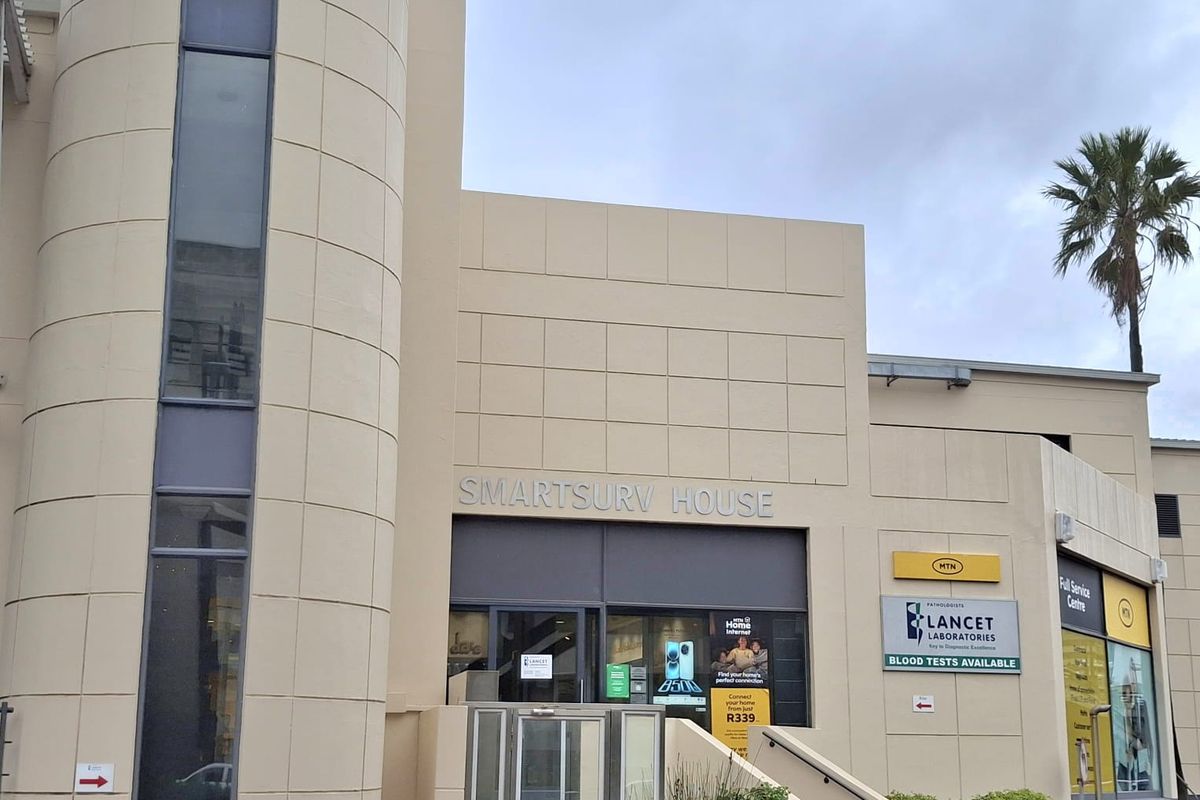 Front facade of Smartsurv House, a commercial office building featuring a prominent cylindrical architectural element, glass entrance, and integrated signage for multiple tenants.