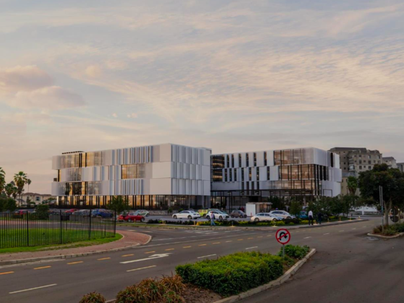 A modern multi-story office building featuring a contemporary glass and panel facade with an adjacent parking area and landscaped surroundings.