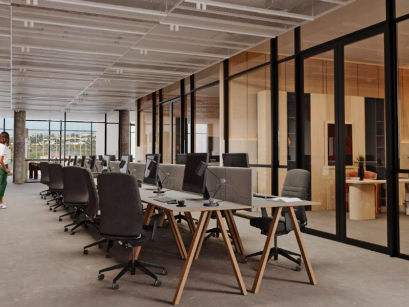 Modern open-plan office space featuring industrial concrete flooring, suspended metal ceiling panels, and floor-to-ceiling glass partitions creating a bright, professional work environment.