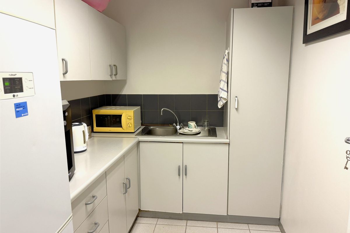 A compact office kitchenette featuring built-in cabinetry, a stainless steel sink, tiled splashback, and laminate countertops.