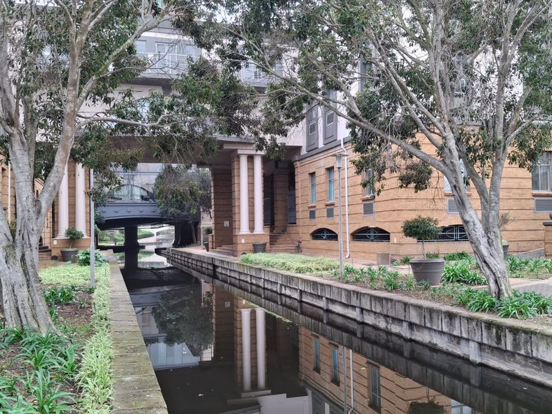 A view of the office building exterior featuring a canal, landscaped garden beds, and architectural brick facade with balconies.