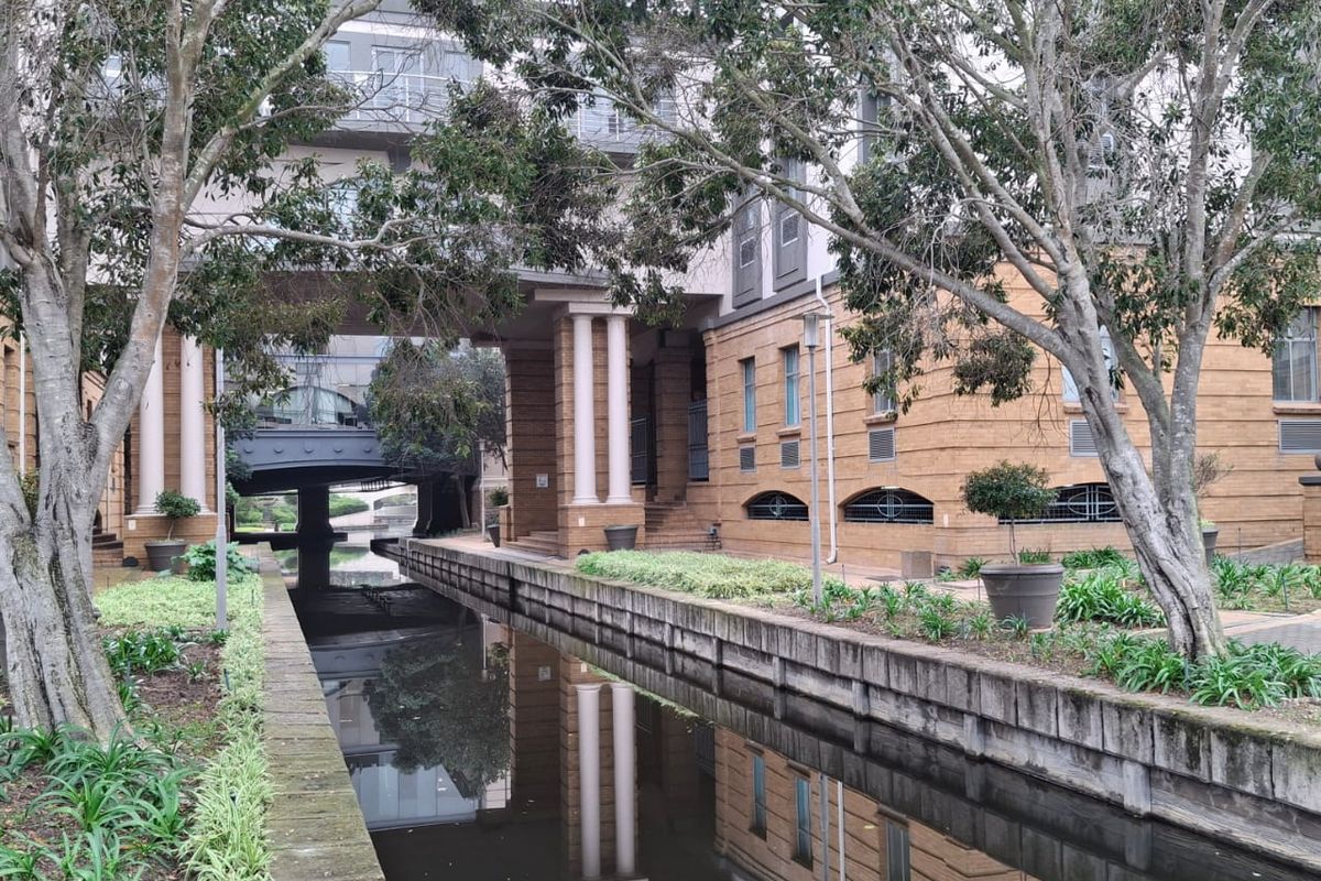 A view of the office building exterior featuring a canal, landscaped garden beds, and architectural brick facade with balconies.
