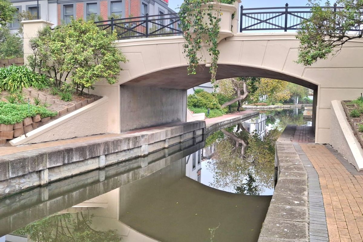 A scenic view of a stone bridge spanning a canal, featuring brick pathways and landscaped retaining walls within the office property grounds.