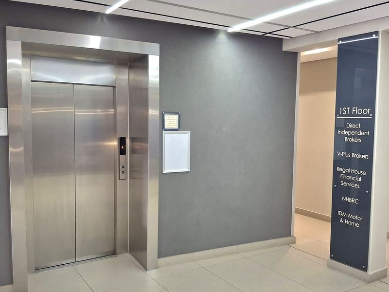 Modern office building lobby featuring a stainless steel elevator, clean tiled flooring, and a professional directory board for first-floor tenants.