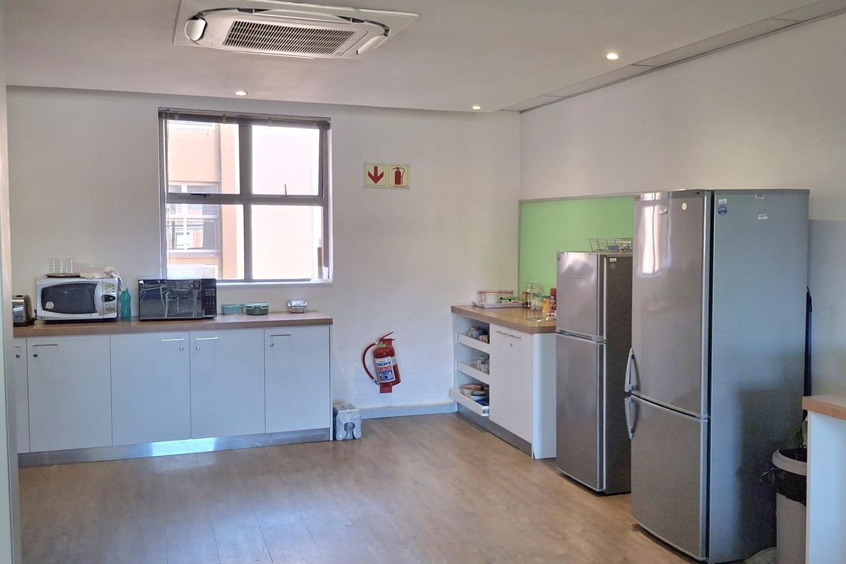 A functional office kitchen area featuring built-in cabinetry, laminate countertops, and a ceiling-mounted air conditioning unit.