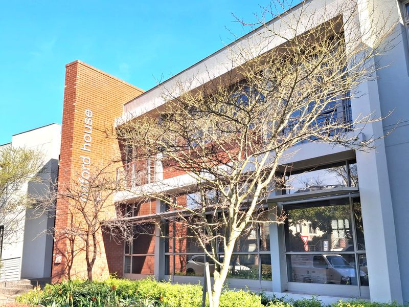 A modern office building exterior featuring a brick facade, large glass windows, and a well-maintained landscaped garden area.