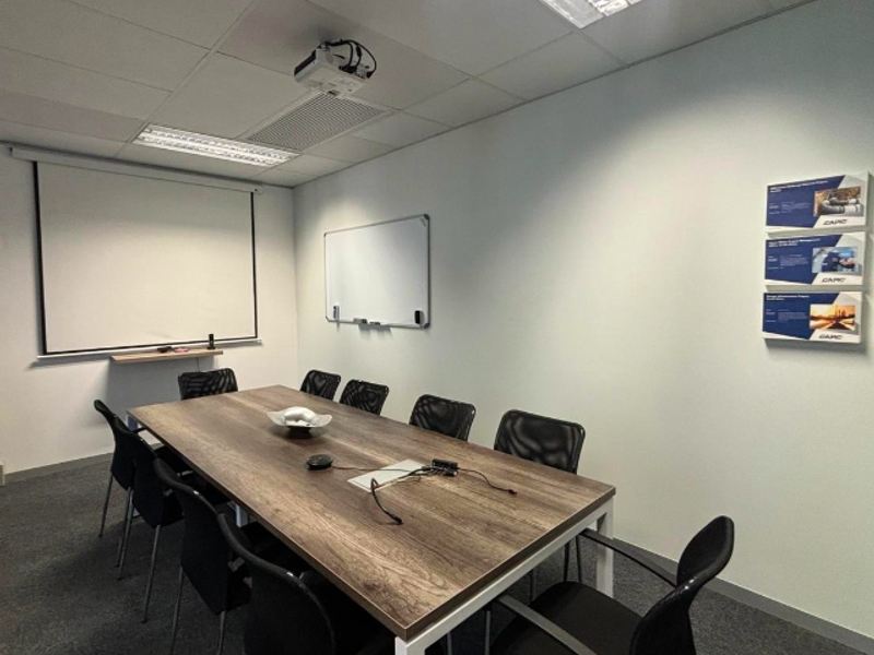 A functional office meeting room featuring a suspended ceiling, recessed lighting, a wall-mounted projector screen, and a whiteboard.