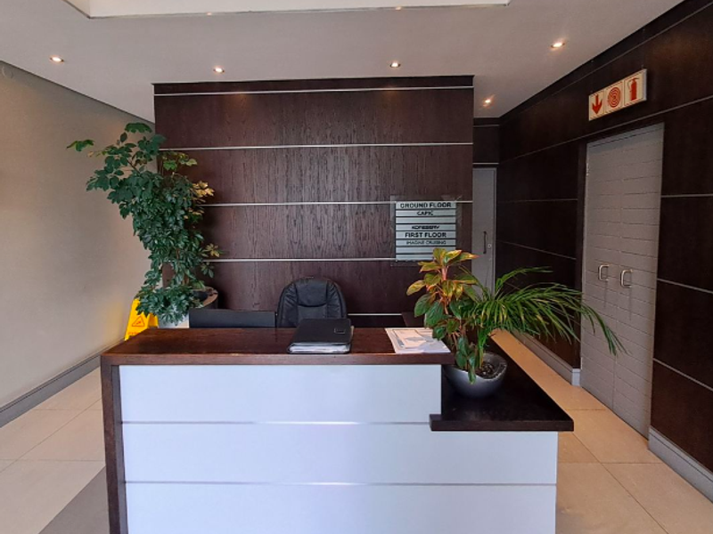 A professional office building entrance featuring a modern reception desk, directory signage, and clean tiled flooring with recessed ceiling lighting.