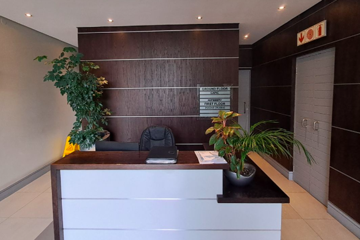 A professional office building entrance featuring a modern reception desk, directory signage, and clean tiled flooring with recessed ceiling lighting.
