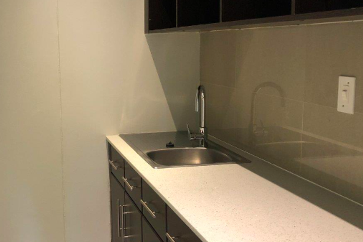 A clean, modern kitchenette featuring dark cabinetry, a stone countertop, stainless steel sink, and overhead storage shelving.