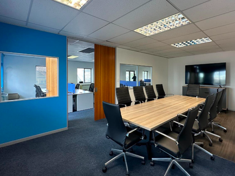 A professional office meeting room featuring a large conference table, suspended ceiling with recessed lighting, and internal glass partitions for an open, connected workspace.