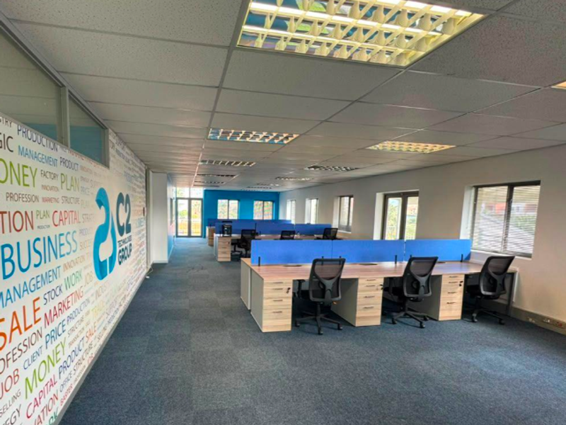 Open-plan office space featuring a suspended ceiling, recessed lighting, carpeted flooring, and large windows providing natural light.