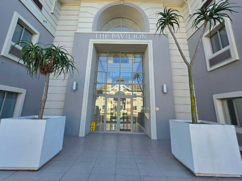 The main entrance to The Pavilion office building, featuring a prominent glass facade, arched architectural detailing, and a clean tiled approach.