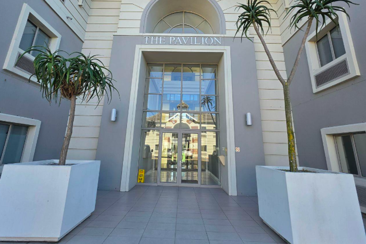 The main entrance to The Pavilion office building, featuring a prominent glass facade, arched architectural detailing, and a clean tiled approach.