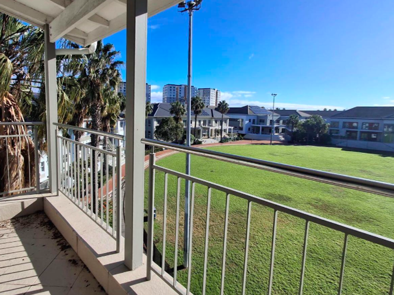A covered balcony with metal railings overlooking a large green field and surrounding office complex buildings.