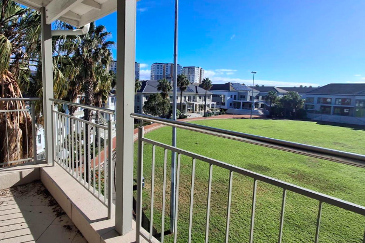 A covered balcony with metal railings overlooking a large green field and surrounding office complex buildings.