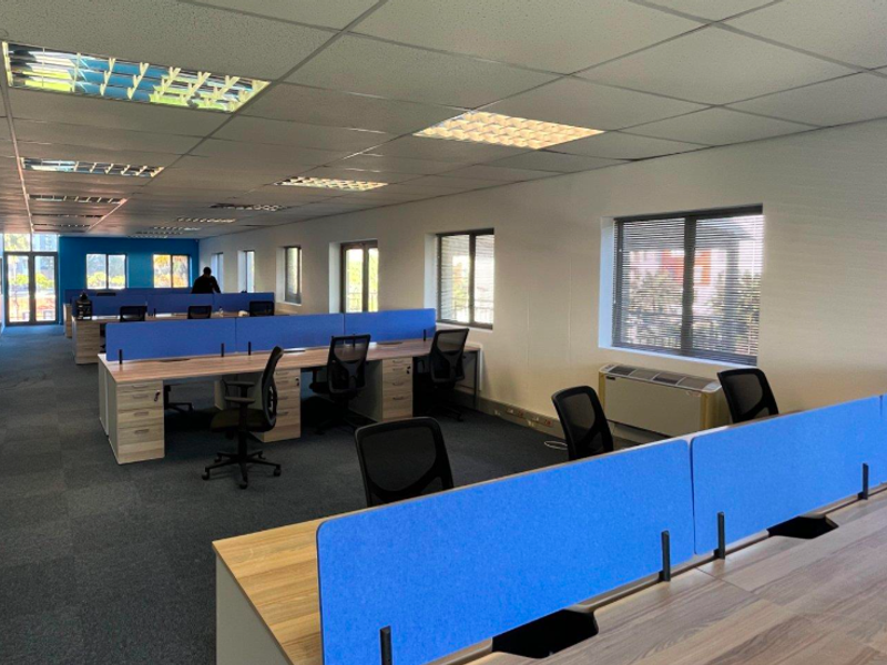 Spacious open-plan office area featuring carpeted flooring, suspended ceilings with recessed lighting, and large windows with fitted blinds.
