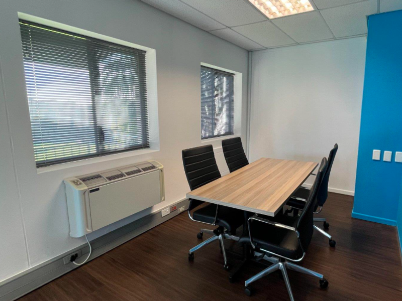 A professional office meeting room featuring laminate flooring, recessed lighting, venetian blinds, and a wall-mounted HVAC unit.