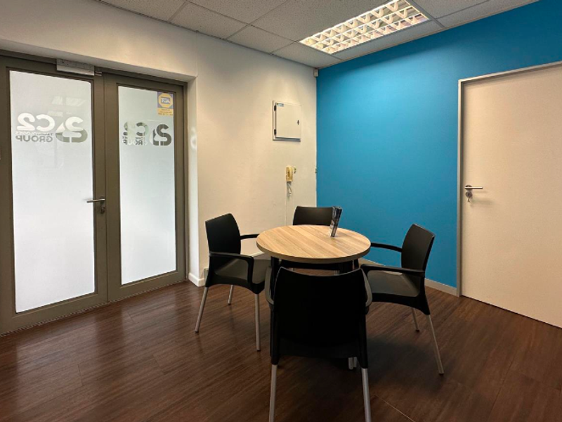 A functional office space featuring laminate flooring, a suspended ceiling with recessed lighting, and a double glass entrance door.