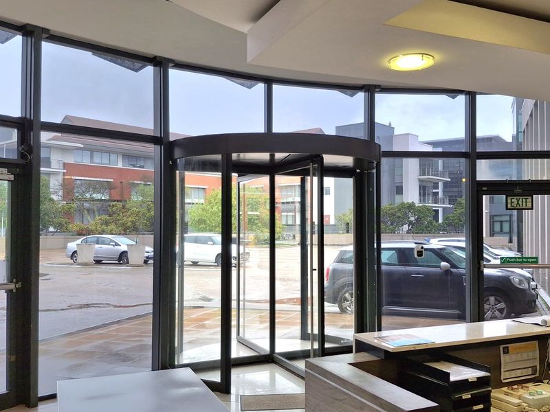 Modern office building entrance featuring a revolving door, floor-to-ceiling glass facade, security turnstile, and a professional reception desk area.