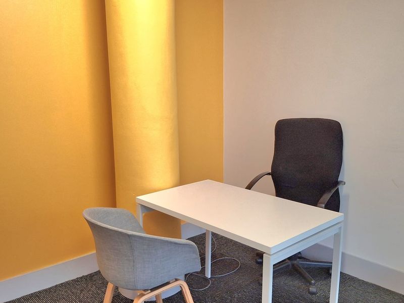 A compact office space featuring a prominent structural column, neutral wall finishes, and durable carpet tile flooring.