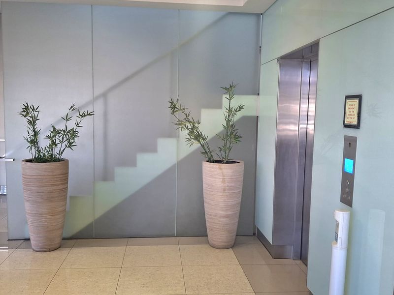 Modern office building lobby entrance featuring a stainless steel elevator, sleek glass wall paneling, and polished tiled flooring with recessed lighting.