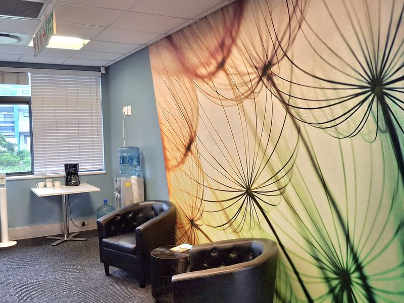 A professional office waiting area featuring carpet tiles, recessed ceiling lighting, and a large decorative wall mural.