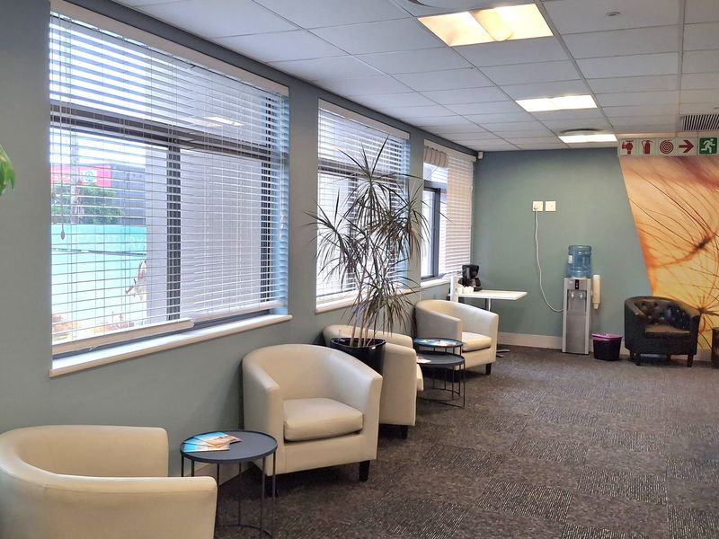 A professional office waiting area featuring carpeted flooring, suspended ceiling with recessed lighting, and large windows with venetian blinds.