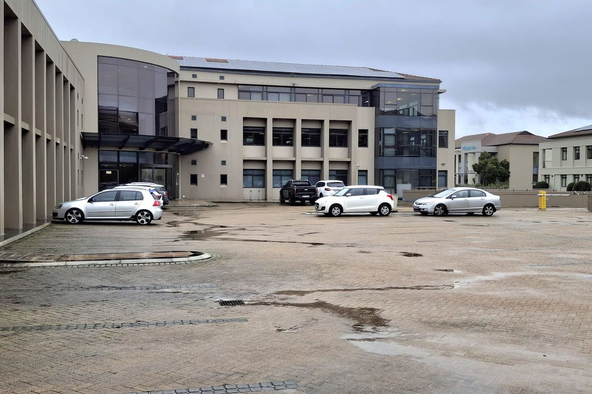 Exterior view of a multi-story office building featuring a paved parking area and modern glass facade elements.