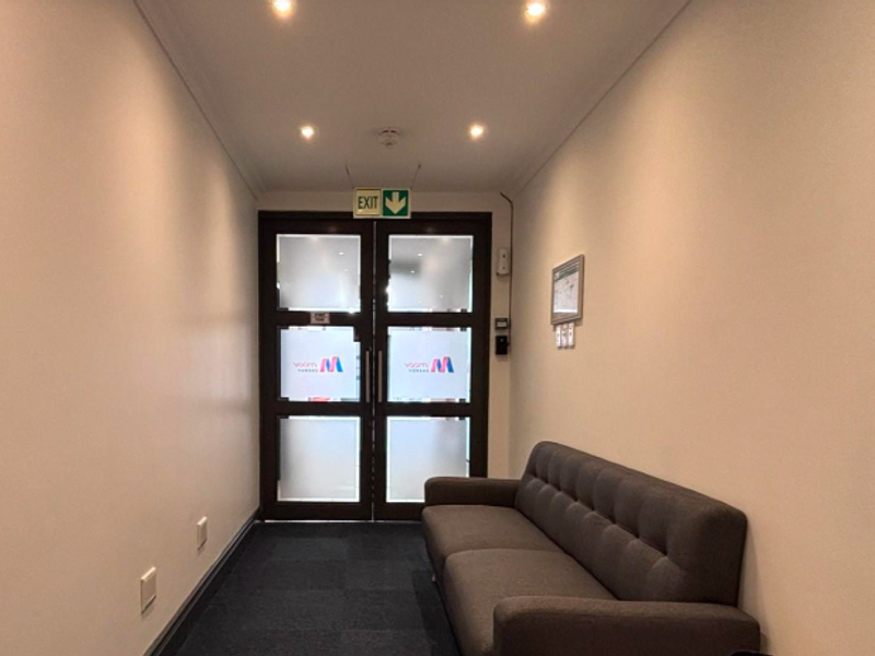 A clean, well-lit office hallway featuring recessed downlighting, carpeted flooring, and frosted glass double doors leading to an exit.