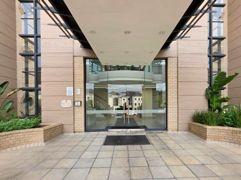 Professional office building entrance featuring a modern glass door system, brick facade, and a covered canopy walkway with integrated lighting.