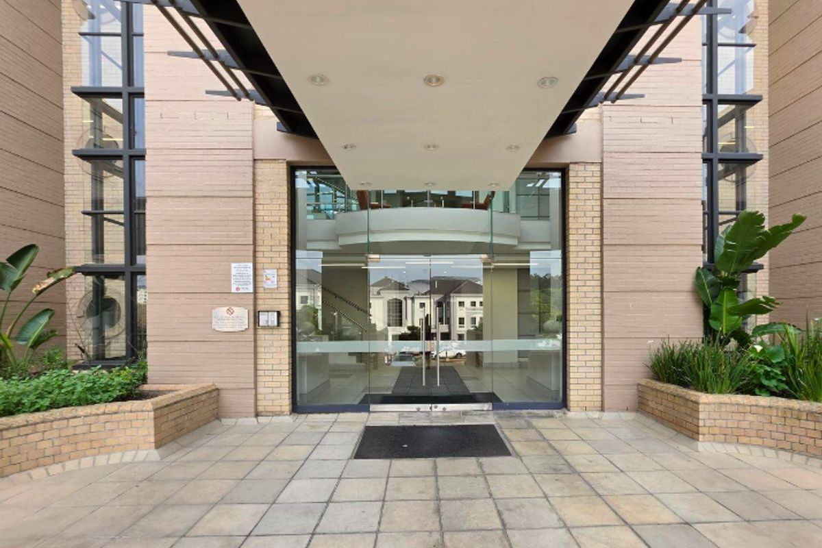 Professional office building entrance featuring a modern glass door system, brick facade, and a covered canopy walkway with integrated lighting.